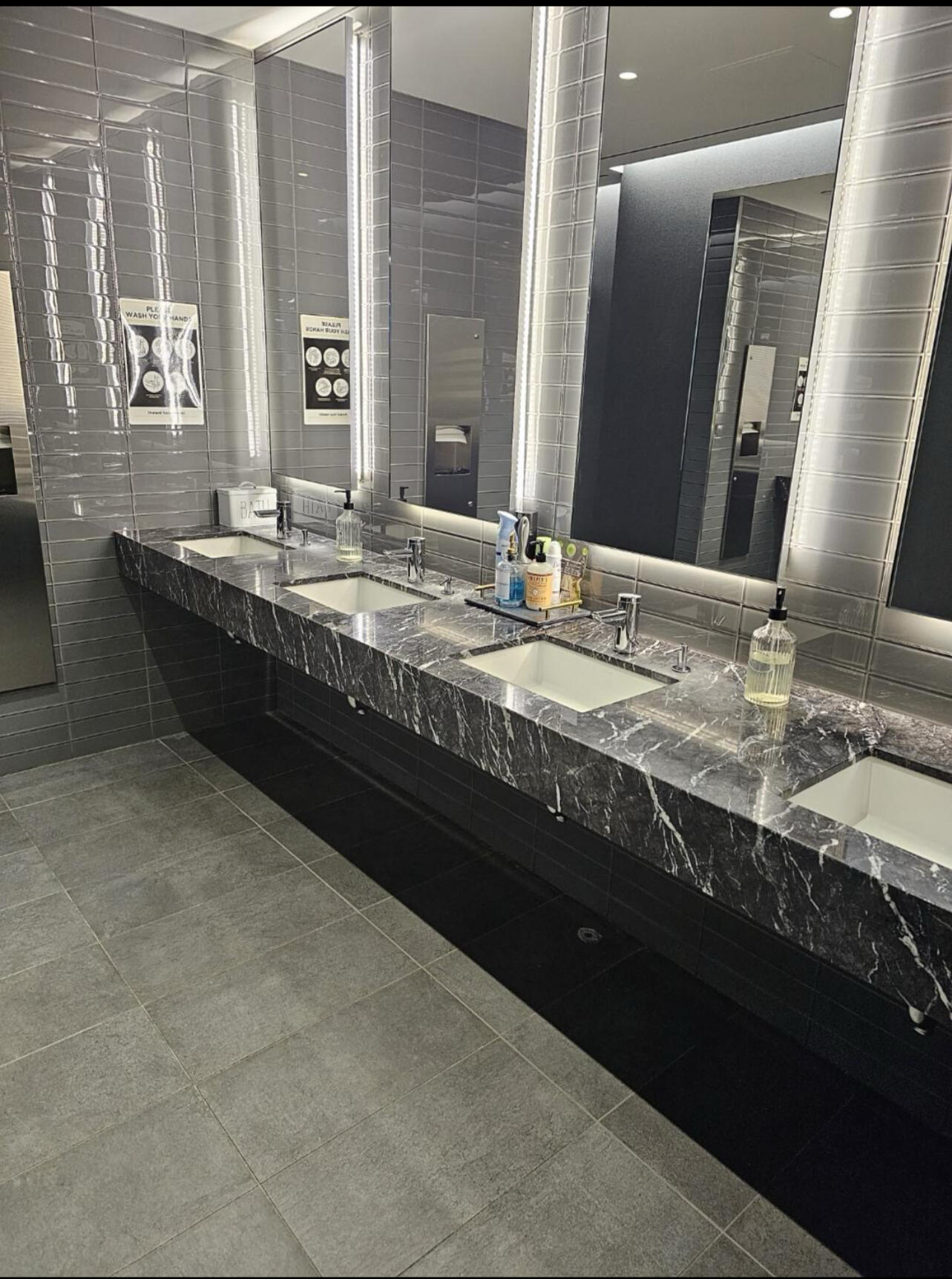 Commercial restroom with polished marble vanity, mirrors, and glass tile